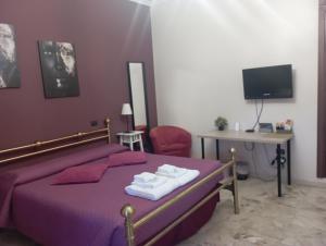 ローマにあるB&B "Feelgood"の紫色のベッド、デスク、テレビが備わるベッドルーム1室が備わります。