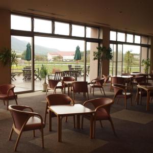 Kyukamura Hiruzen-Kogen في Maniwa: غرفة بها طاولات وكراسي ونافذة كبيرة