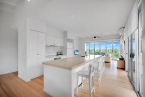 a kitchen with white cabinets and a bar with white stools at 2 Casuarinas Peregian Beach in Coolum Beach