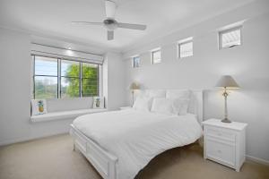 a white bedroom with a white bed and a window at 2 Casuarinas Peregian Beach in Coolum Beach