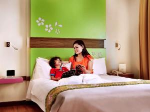 una mujer y un niño acostados en la cama con una tableta en Ibis Styles Bali Denpasar en Denpasar