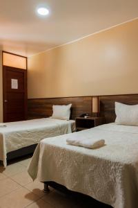 Habitación de hotel con 2 camas con sábanas blancas en Hotel El Huacachinero en Ica