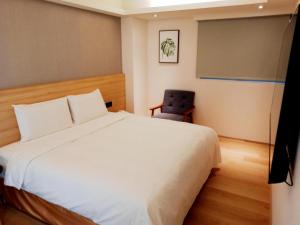 um quarto com uma cama branca e uma cadeira em Fooyee Hotel - Yonghe em Yonghe