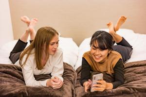 Due donne stese su un letto che guardano un cellulare di Cominka Yufuin a Yufu