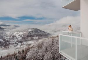 a woman standing on a balcony taking a picture of a snowy mountain at Crystal Mountain Hotel Wisła in Wisła