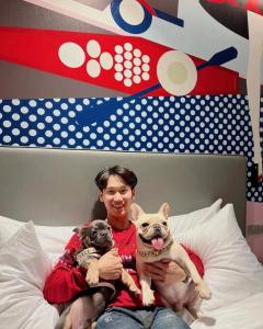 a man sitting on a bed holding two dogs at Oakwood Studios Sukhumvit Bangkok in Bangkok