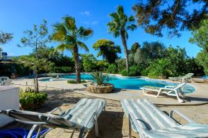 una piscina con 2 sillas de césped y palmeras en Villa Can Sarrio, en Sant Carles de Peralta