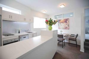 Central Hobart - Beautiful Apartment في هوبارت: مطبخ أبيض مع إناء من الزهور على منضدة