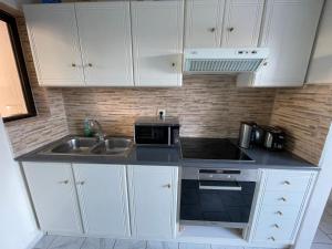 a kitchen with white cabinets and a sink and a microwave at Tersanas Beach Apartments in Chorafakia