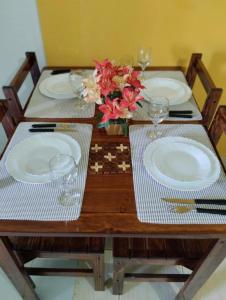 a wooden table with plates and glasses and flowers on it at Apartamento cercado por natureza e diversão in Maceió