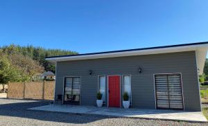 una pequeña casa con puerta roja y 2 sillas en Cabañas Los Robles, en Coelemu