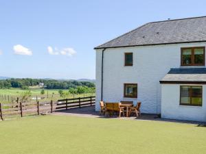 a white house with a table and chairs next to a field at The Byre Camp Douglas in Crossmichael