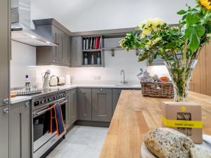 una cocina con armarios grises y una mesa con un jarrón de flores en Church Garden Cottage en Higham