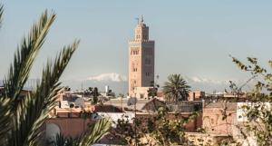 einen Uhrturm in einer Stadt mit Bergen im Hintergrund in der Unterkunft Palais Riad Lamrani in Marrakesch
