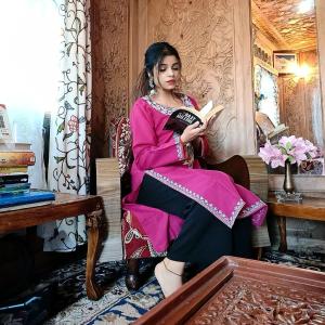 una mujer sentada en una silla leyendo un libro en Lala Rukh Group Of Houseboats en Srinagar