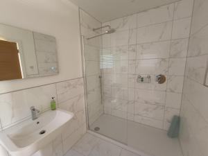 a white bathroom with a shower and a sink at Petite Anchorage in Christchurch