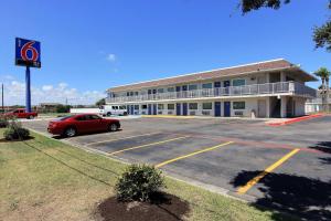 un edificio con una macchina rossa parcheggiata in un parcheggio di Motel 6-Corpus Christi, TX - East - North Padre Island a Corpus Christi