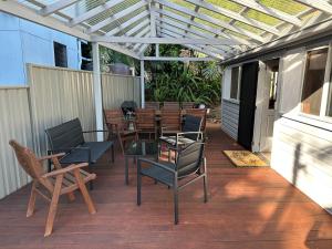un patio con sillas, mesas y una pérgola en Patonga Holiday Home, en Patonga