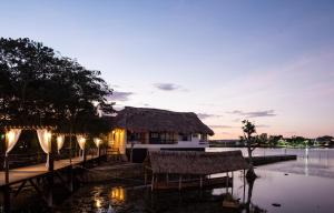 ein Haus mit einem Strohdach neben einem Wasserkörper in der Unterkunft Maya Internacional in Flores