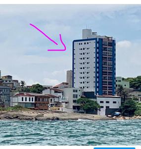 a tall building with a pink arrow in front of a city at Apartamento Pé na Areia e águas tranquilas no centro de Guarapari in Guarapari
