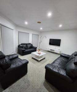uma sala de estar com mobiliário de couro preto e uma televisão de ecrã plano em Daisy Villa em Warrnambool