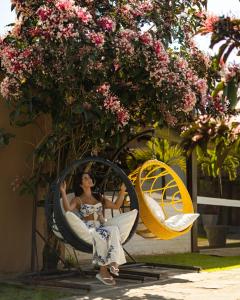 a woman sitting in a wicker chair under a tree at Pousada Algodão da Praia in Araruama