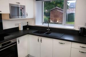cocina con armarios blancos, fregadero y 2 ventanas en Central 2 bedroom luxury home close to River Ness, en Inverness