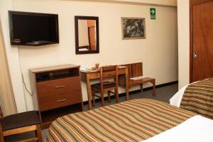 ワンカヨにあるHotel Presidente Huancayo - Asociado Casa Andinaのデスク、テーブル、ベッドが備わる客室です。