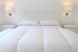 a white bed with white sheets and two night stands at Luces de la Paloma in La Paloma