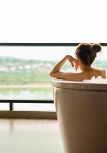 a woman sitting in a bath tub in front of a window at Chiangkhong Teak Garden Riverfront Onsen Hotel- SHA Extra Plus in Chiang Khong