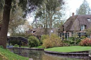 a house with a thatched roof next to a river at Appartement Hoek in Giethoorn