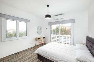 a white bedroom with a bed and two windows at Happy Stay Apartment - Halefka Court in Larnaka