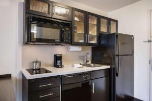 a kitchen with black cabinets and a stainless steel refrigerator at Sonesta Simply Suites Chicago O'Hare Airport in Schiller Park