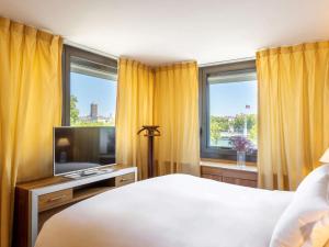 a bedroom with a bed and a tv and windows at Sofitel Lyon Bellecour in Lyon