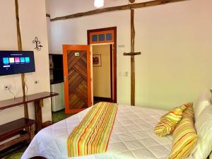 a bedroom with a bed and a tv and a door at Gaia Gardens Pousada in Paraty