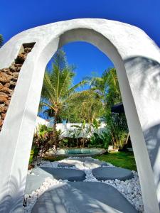 um arco de pedra que leva a um jardim com palmeiras em Pousada Ilha do Vento em São Miguel do Gostoso