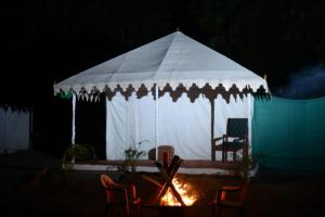 a white tent with chairs and a fire in the dark at River View Tent Resort in Garudeshwar