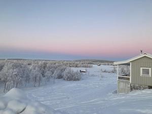 a house in the snow with a field and trees at Kuttainen Lodge in Karesuando