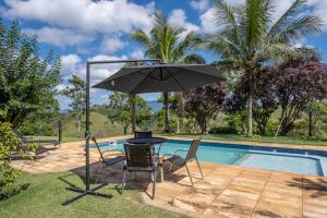 a table and chairs with an umbrella next to a pool at Sítio Paraíso Beach Tennis in Vassouras +29 photos