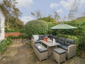 a patio with a couch and a table and an umbrella at Mackerel Cottage in Budleigh Salterton