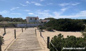 una passerella di legno su una spiaggia con un edificio di Apto Mar de Es Caló, a metros de la playa - Formentera Natural a Es Caló de Sant Agustí