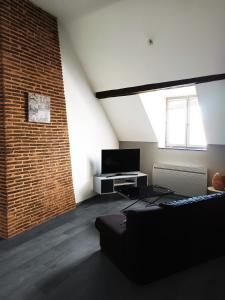 Habitación con sofá, TV y pared de ladrillo. en Appartement chaleureux en Mirebeau-sur-Bèze