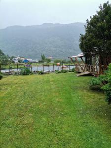 une cour herbeuse avec une maison et une masse d'eau dans l'établissement Departamento Rossbach, à Puerto Puyuhuapi