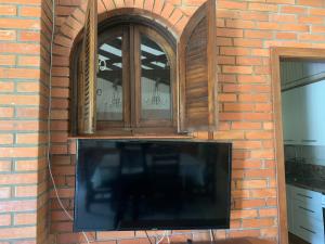 TV en una pared de ladrillo con 2 ventanas en Sítio Vale dos Vinhedos, en Bento Gonçalves