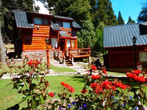 una cabaña de madera con flores rojas delante de ella en LADERAS DEL CAMPANARIO en San Carlos de Bariloche