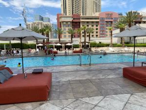 a swimming pool with two red couches and umbrellas at Balcony Suite Strip View in Las Vegas