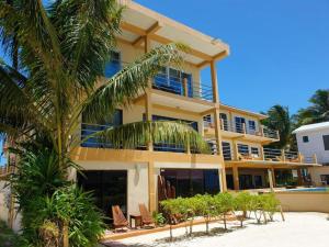a large yellow building with chairs and a palm tree at Beach Side Condos Caye Caulker by CCVH in Caye Caulker