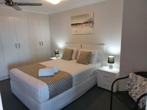 a bedroom with a white bed with two lamps and a chair at Sandy Shores Holiday Units in Caloundra