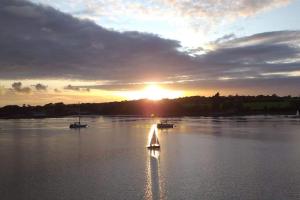 a sail boat in the water with the sun setting at 'Ar Y Tonnau' Y Felinheli Waterside Apartment in Y Felinheli