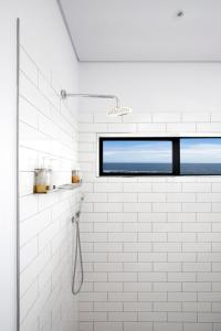 a white tiled bathroom with a window and a shower at OnTheRocksBB Solar Powered Guesthouse and Ocean Lodge in Bettyʼs Bay